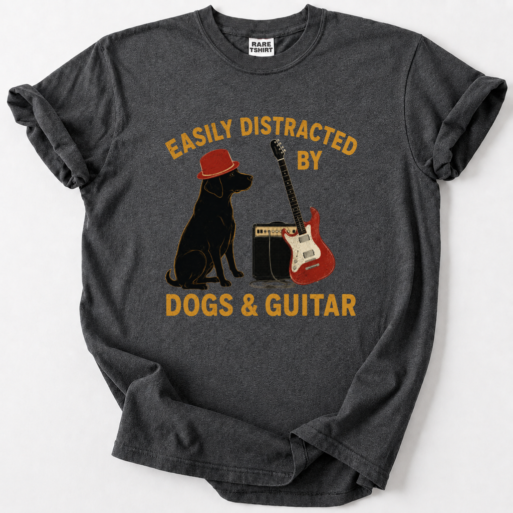 A dark gray heather t-shirt with a graphic print of a black dog wearing a red hat, a red electric guitar, and a speaker, with the text 'EASILY DISTRACTED BY DOGS & GUITAR' in yellow. The shirt is laid flat on a light gray background.