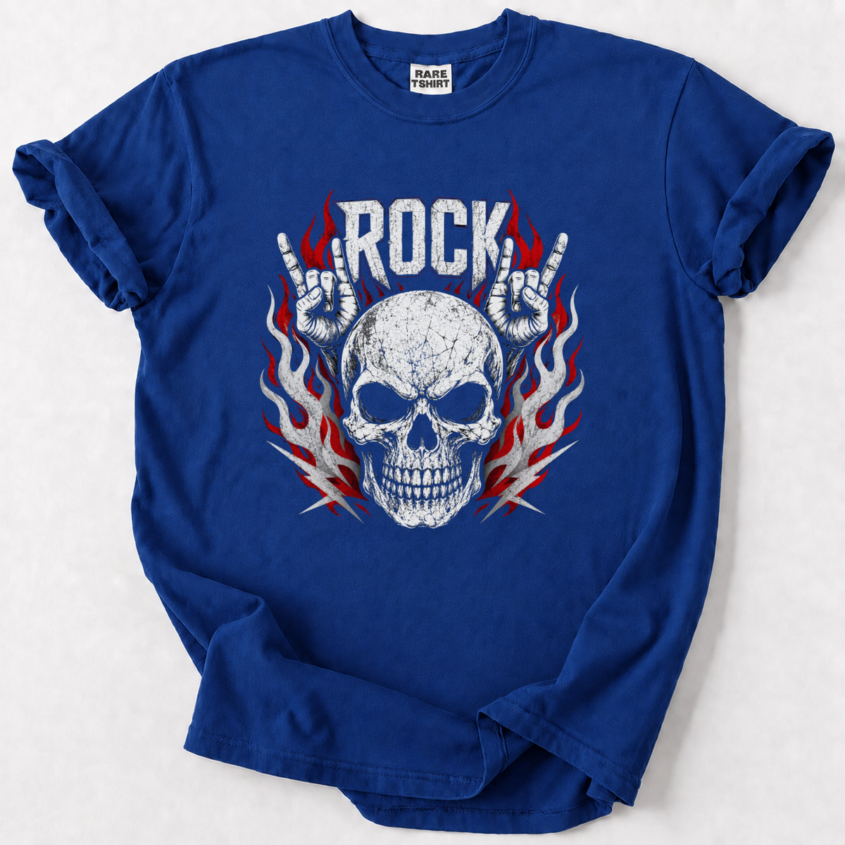 A royal blue short-sleeve t-shirt with a graphic print of a skull, flames, and hands making the rock gesture, with the word 'ROCK' above. The shirt is laid flat on a light gray background.