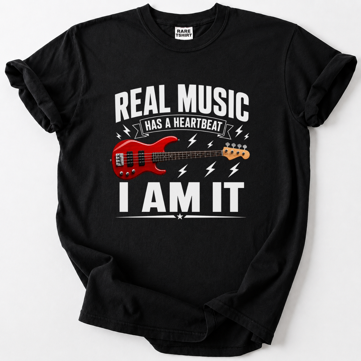 A black short-sleeve graphic t-shirt laid flat on a light gray background. The shirt features a white text graphic reading 'REAL MUSIC HAS A HEARTBEAT I AM IT' surrounding an illustration of a red electric bass guitar.