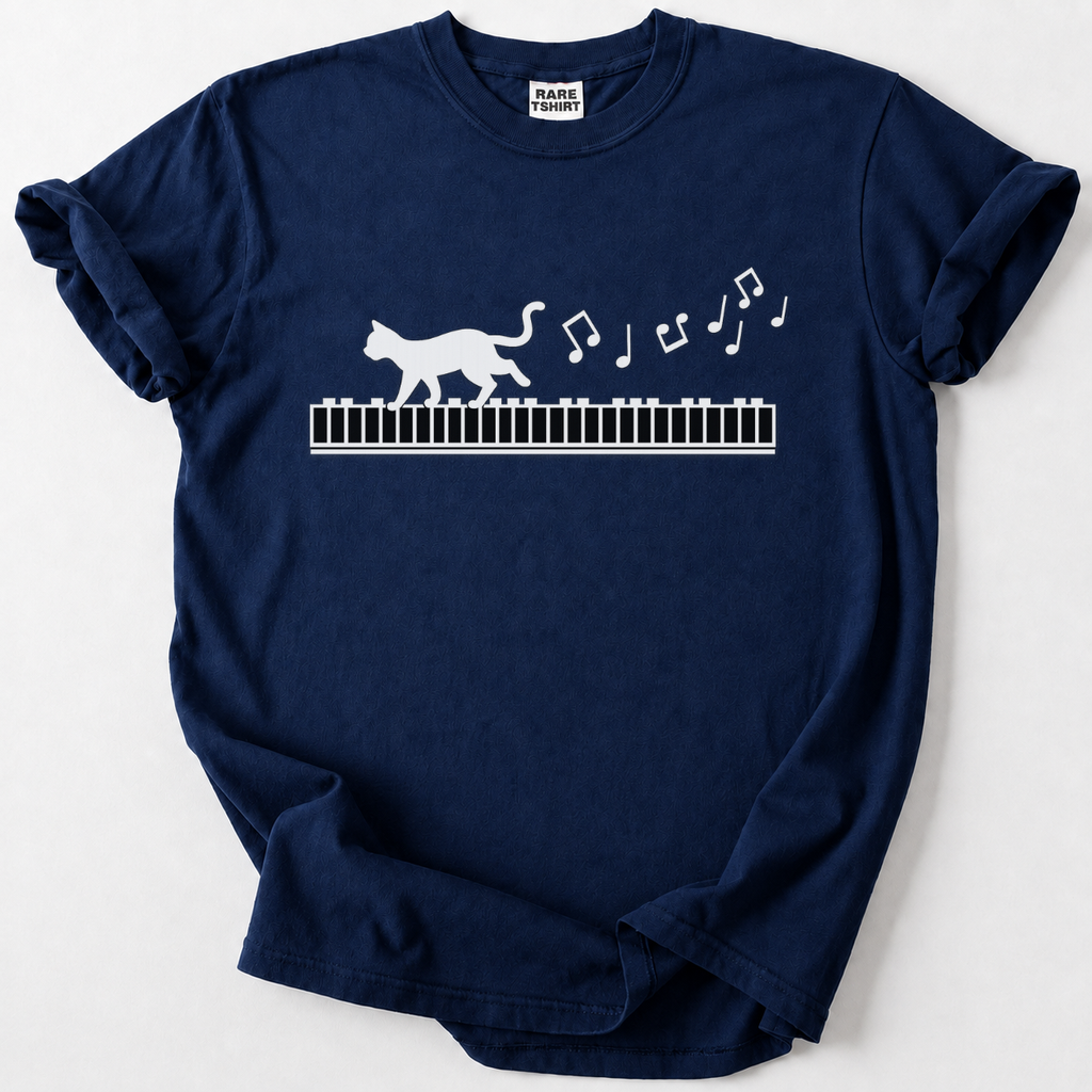 A navy blue short-sleeve t-shirt with a white graphic of a walking cat on a piano keyboard and floating musical notes, laid flat on a light gray background. The neck label shows the brand 'PARKS PRINTS'.